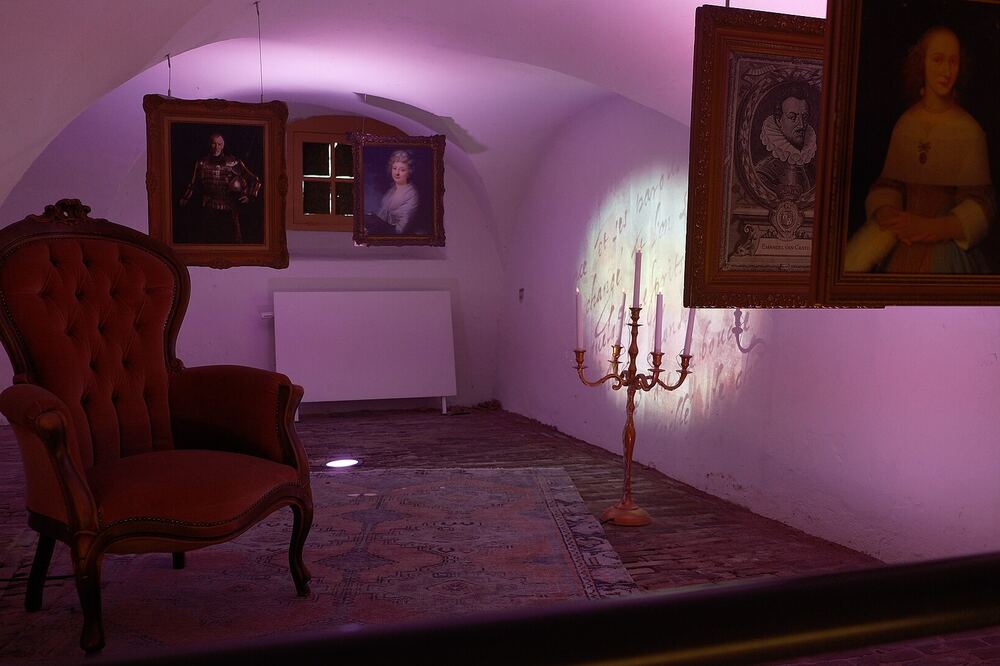 Gewelfde kelderzaal van Kasteel Wijchen met historische portretten aan de wand, een rode fauteuil en sfeerverlichting